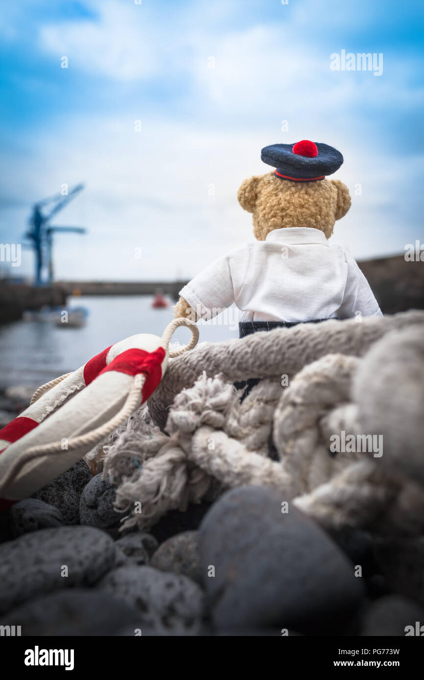 Little sailor Teddybär sitzen am Hafen, schaut in Richtung Meer, voller Gefühle, weg von zu Hause (Kopie) Stockfoto