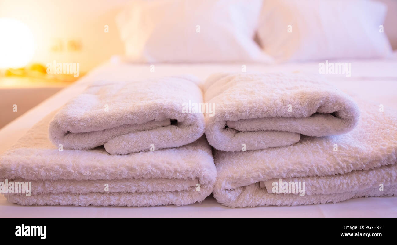 Hotel Zimmer Konzept. Close-up gestapelt, weiße Handtücher auf dem Bett auf einem Unscharf warm beleuchteten Hintergrund Stockfoto