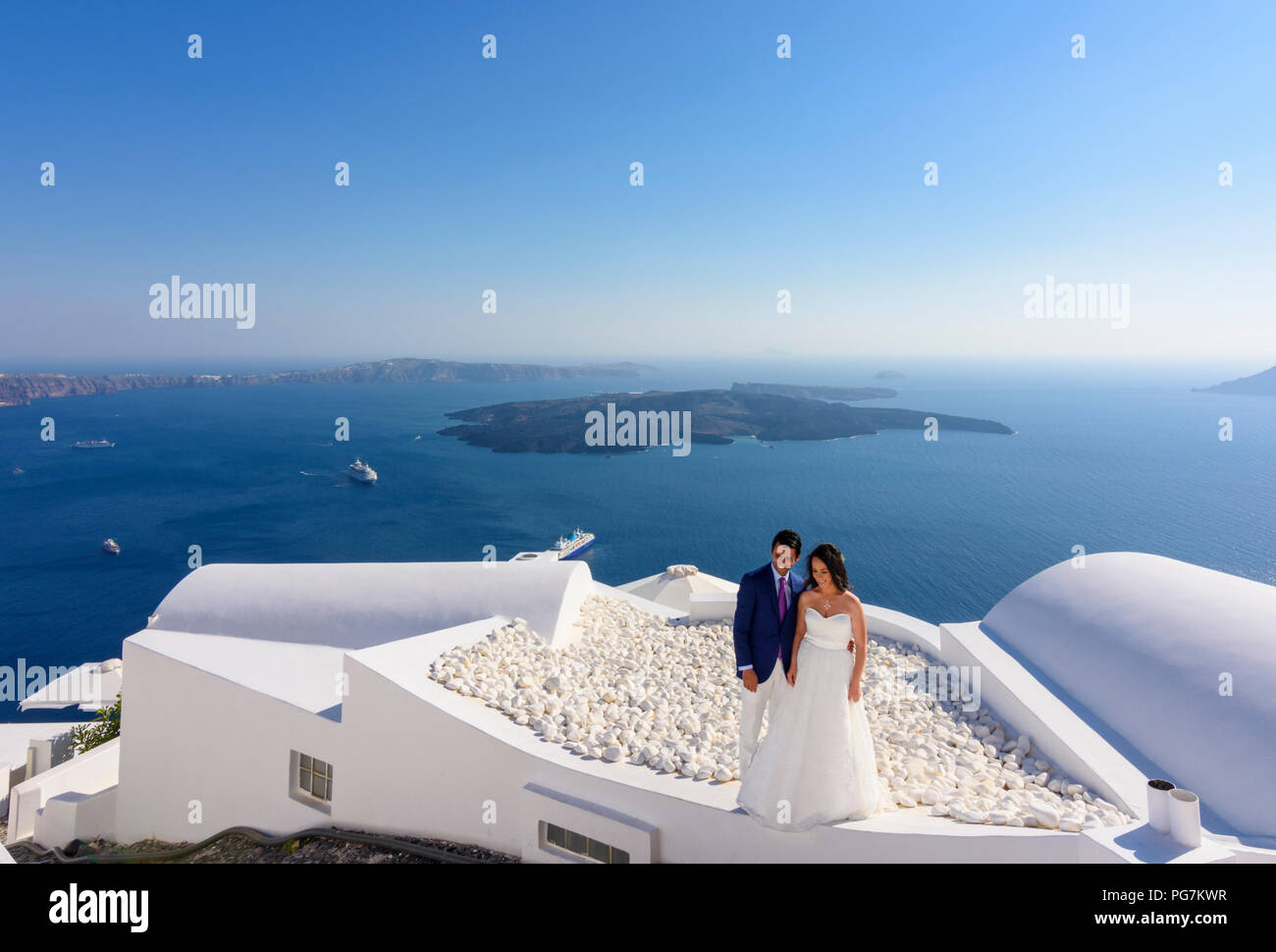 Ein Hochzeitspaar Pose auf der Dachterrasse von einem weiß getünchten Gebäude mit Blick auf die Caldera von Santorin Stockfoto