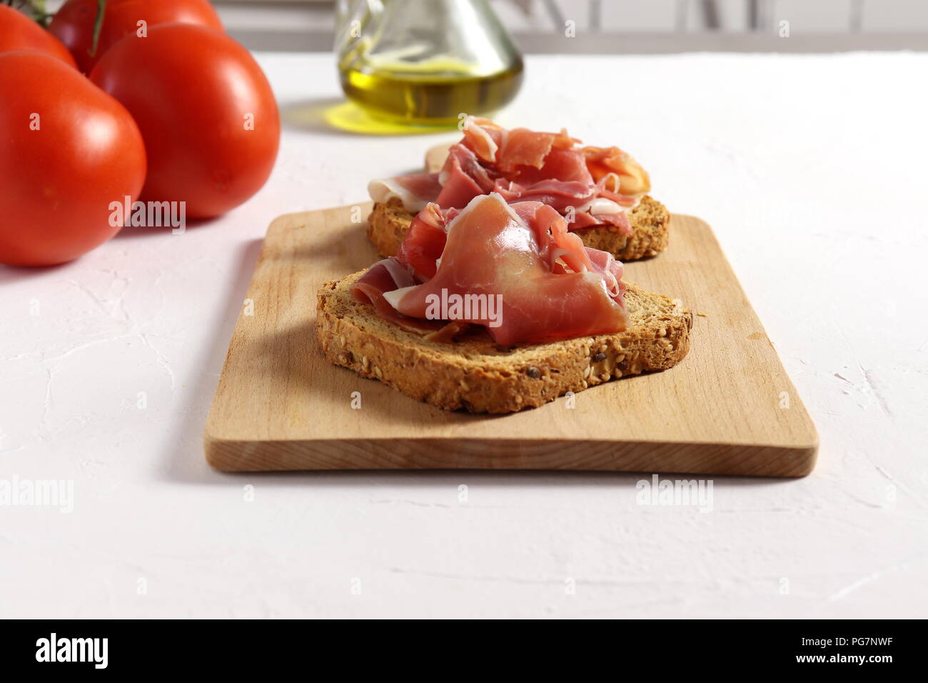 Spanischen Schinken (Jamón) auf ein stück geröstetes Vollkornbrot, Tomaten und Olivenöl neben Stockfoto