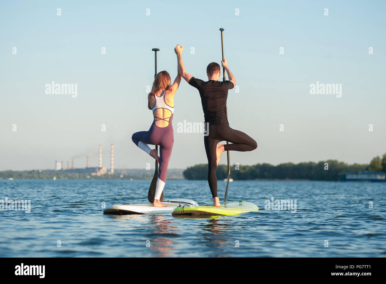 Stand Up Paddle Board Yoga durch schöne Paar auf dem hellen Hintergrund durchgeführt, Yoga Training am Strand Stockfoto