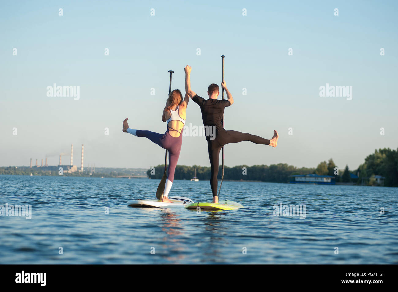 Stand Up Paddle Board Yoga durch schöne Paar auf dem hellen Hintergrund durchgeführt, Yoga Training am Strand Stockfoto