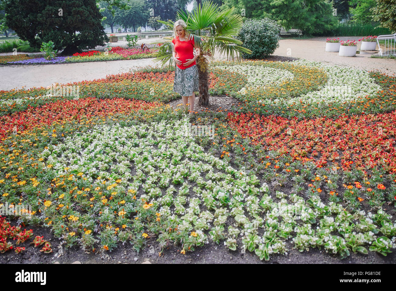 Schwangere Frau steht man inmitten blühender Blumen im Park Stockfoto