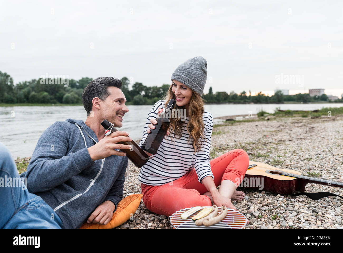 Glückliches Paar entspannende am Flußufer klirren Bier Flaschen Stockfoto