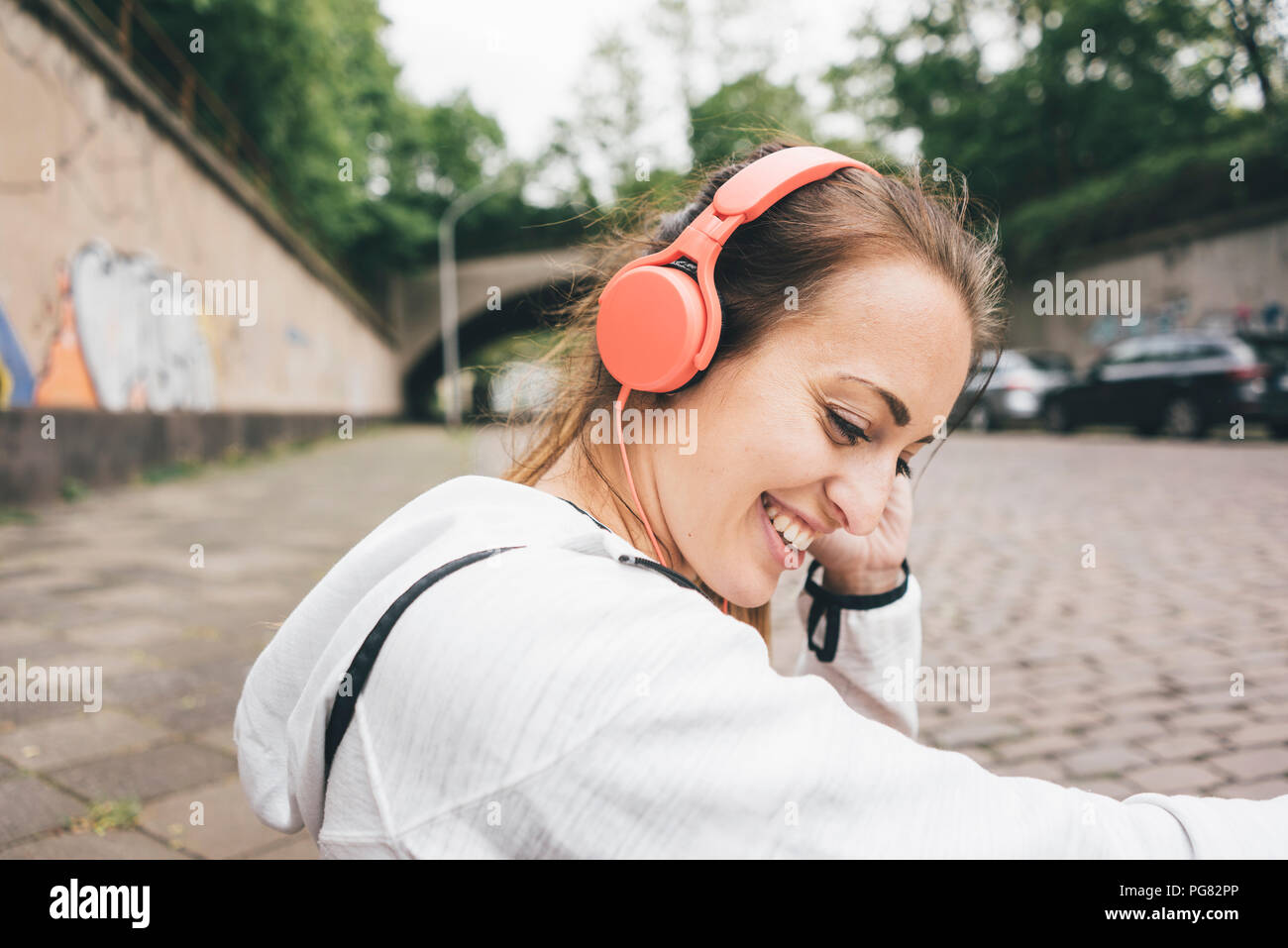 Lächelnd sportliche junge Frau mit Kopfhörern im Freien Stockfoto