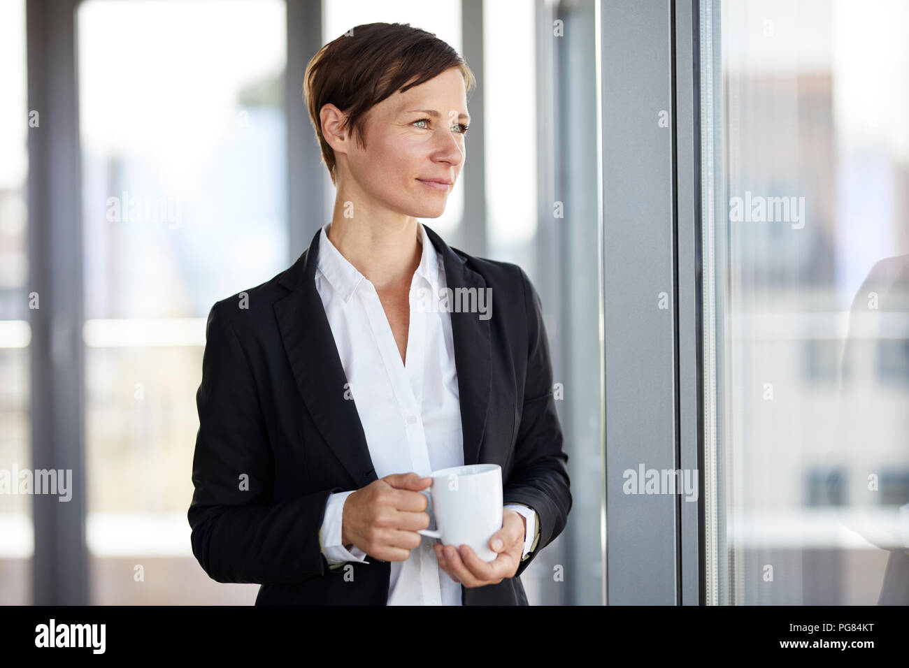 Im Büro mit Tasse Kaffee Blick aus Fenster Geschäftsfrau Stockfoto