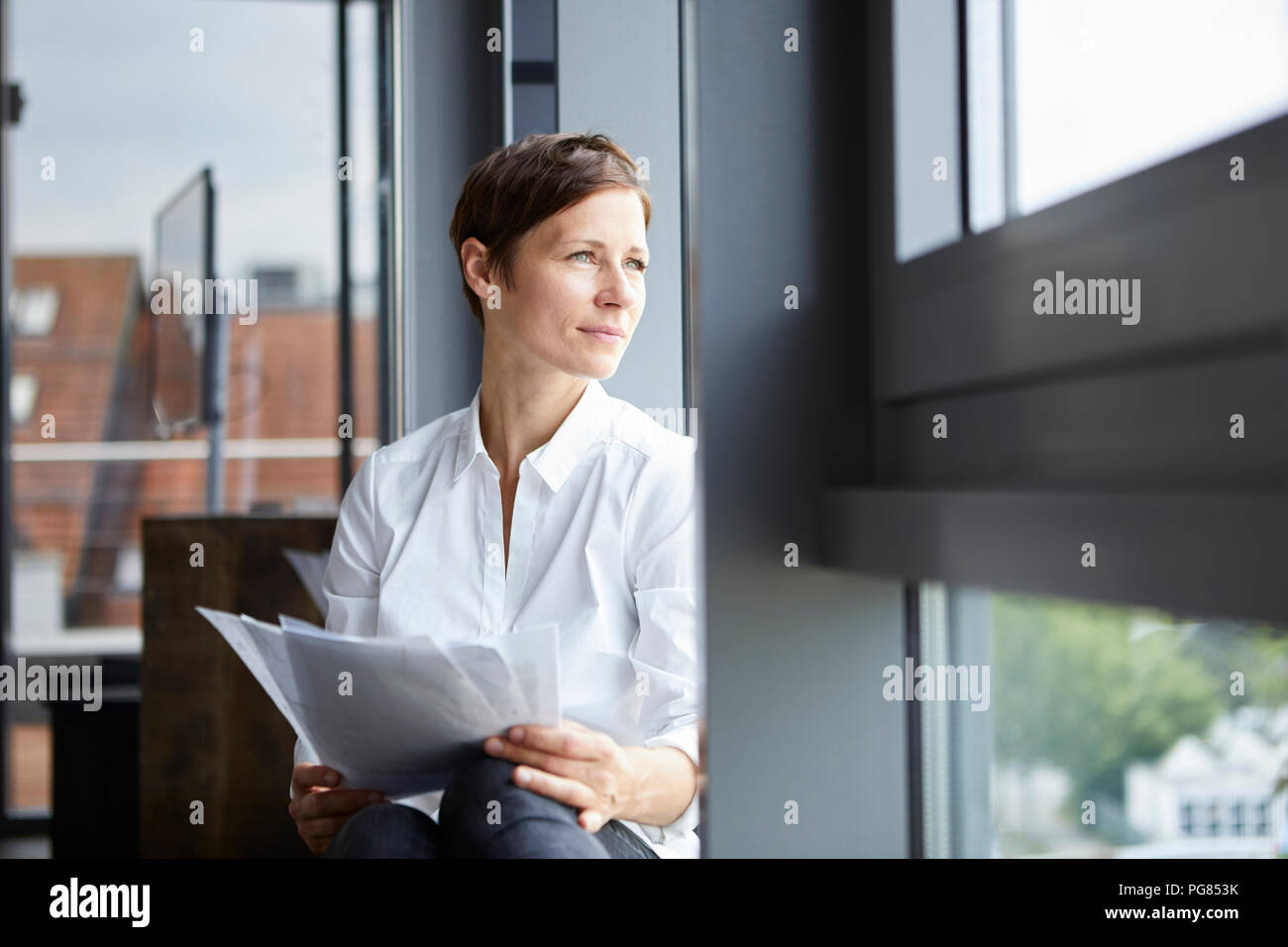 Geschäftsfrau im Büro mit Dokumenten aus Fenster Stockfoto