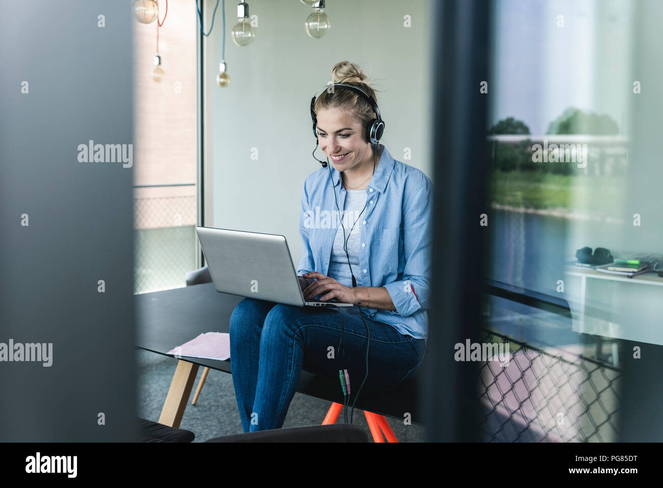 Junge geschäftsfrau am Schreibtisch sitzend, einen Anruf zu tätigen, die mit dem Headset und Laptop Stockfoto