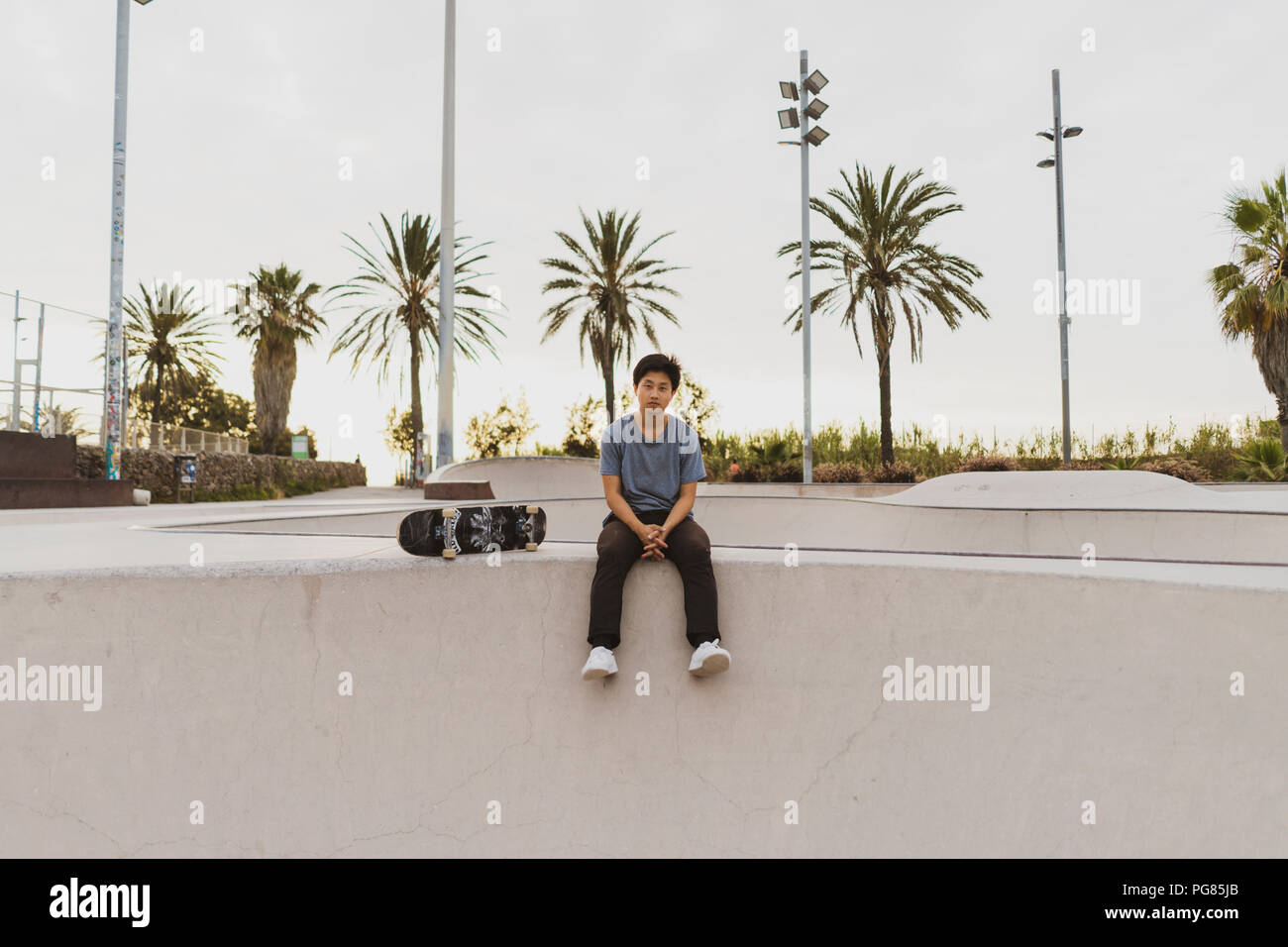 Junge chinesische Mann sitzt auf die Wand von einem Skate Park in der Nähe des Strandes Stockfoto