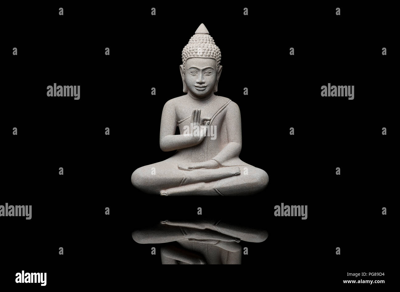 Eine Buddha-Statuette aus hellgrauem Stein, sitzend und schweben vor schwarzem Hintergrund, mit der linken Hand eine Geste, die den Frieden symbolisiert Stockfoto