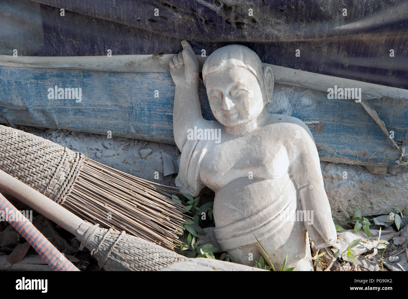 In der Nähe von einem kleinen weißen Marmor Buddha Figur unter staubigen Besen verworfen und Müll in Mandalay, Myanmar Stockfoto