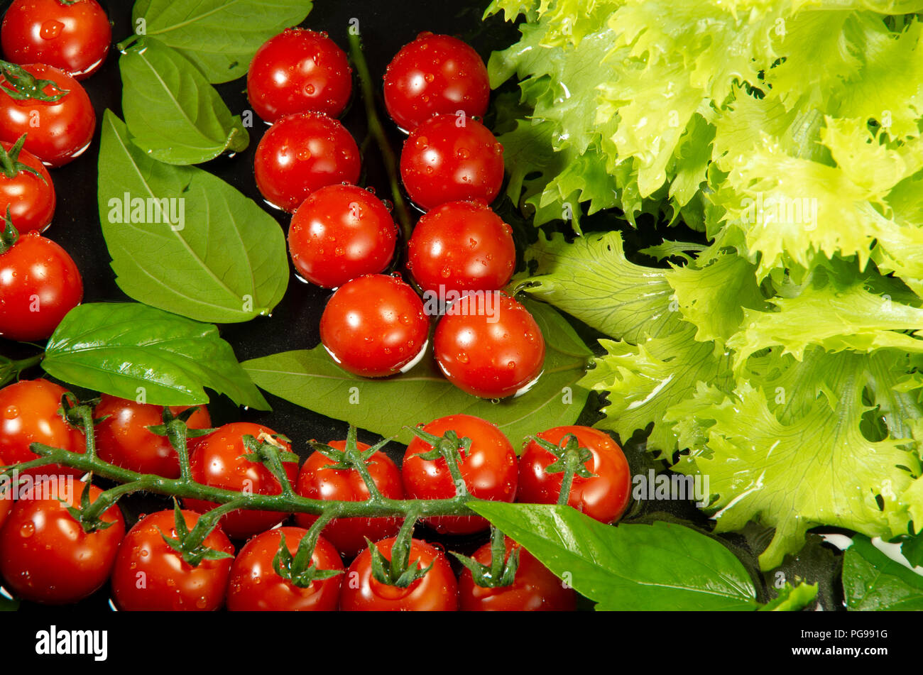 Cherry Tomaten und Kopfsalat in Wasser zum Waschen, Ansicht von oben auf einem dunklen Hintergrund Stockfoto