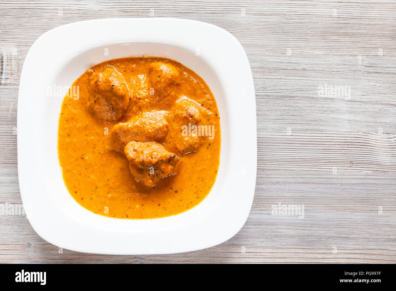 Indische Küche - Murg Makhan Masala gegrillten Hähnchen Stücke in pikanter Tomaten- und cremige Soße Curry in Weiß Schüssel auf hölzernen Tisch Stockfoto