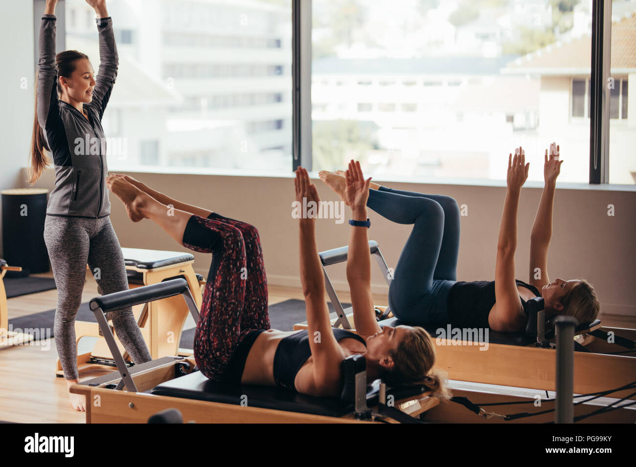 Zwei fitness Frauen, Pilates Übungen heben ihre Hände an einer Turnhalle. Frauen liegen auf Pilates Workout Maschinen während der Trainer führt Sie. Stockfoto