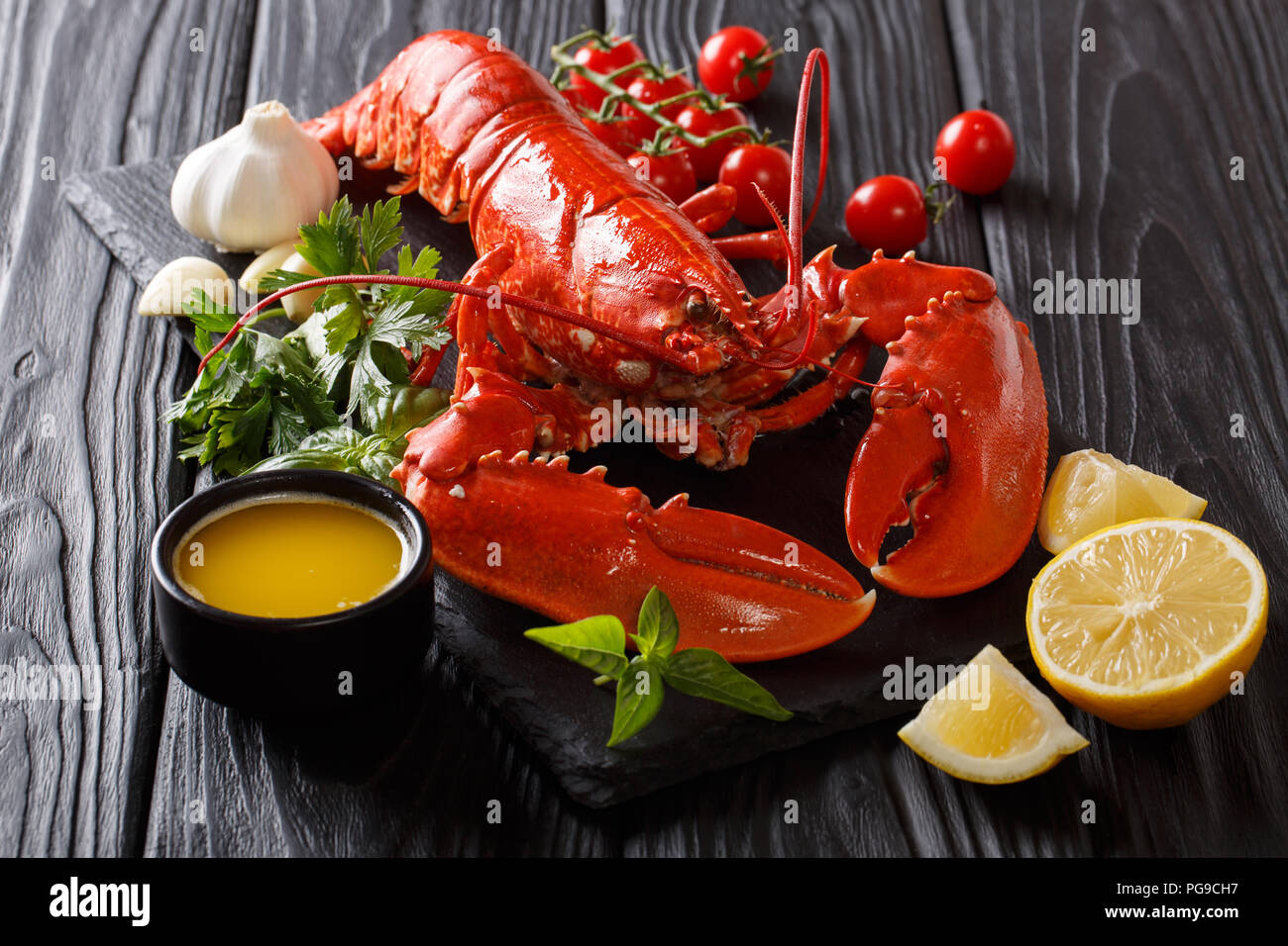 Ganze Red Lobster mit frischer Petersilie, Basilikum, Zitrone, Knoblauch, Tomaten und Butter Nahaufnahme auf dem Tisch. Horizontale Stockfoto