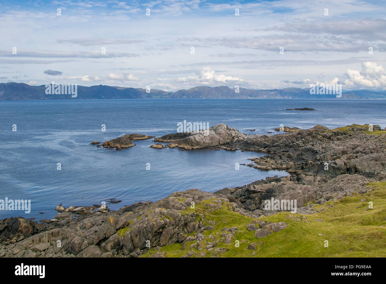 Küsten Norwegen. Ruhige Szene von natürlicher Schönheit. Felsige Küstenlinie, blau bewölkter Himmel, Berge am Horizont. Stockfoto