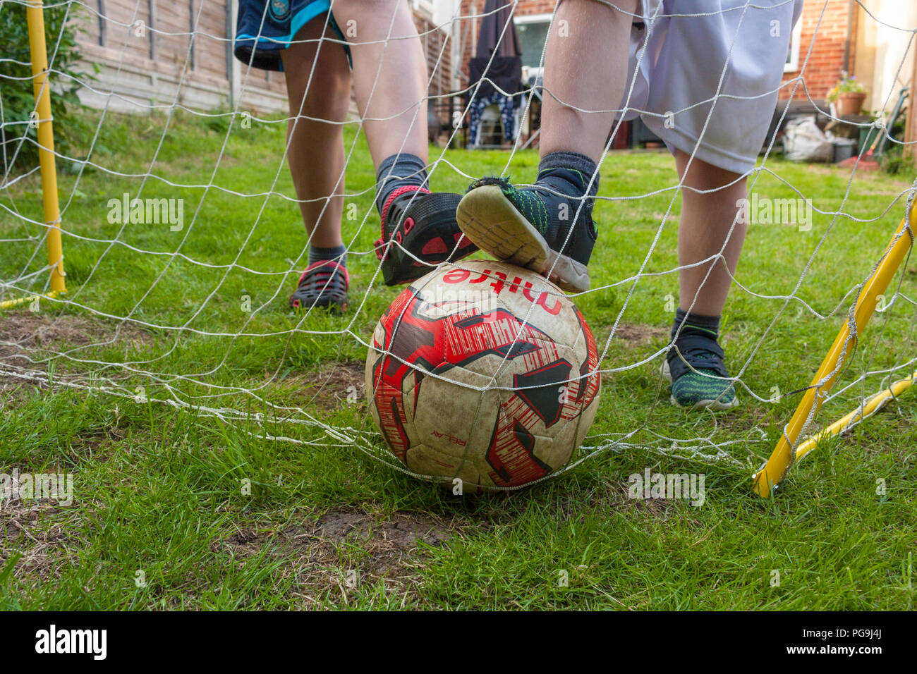 Zwei Jungen mit ihren Füßen auf einen Fußball mit dem Ziel, in einem Garten auf der Rückseite Stockfoto