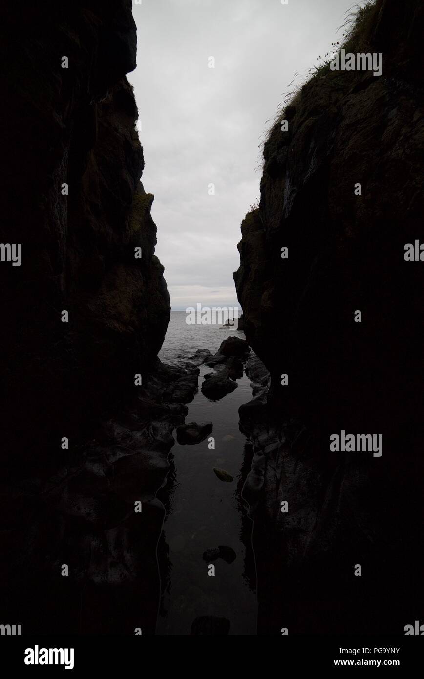 Blick aus der Höhle zu einem Strand an einem bewölkten Tag. Steine und Geologie entlang der Küste. Stockfoto