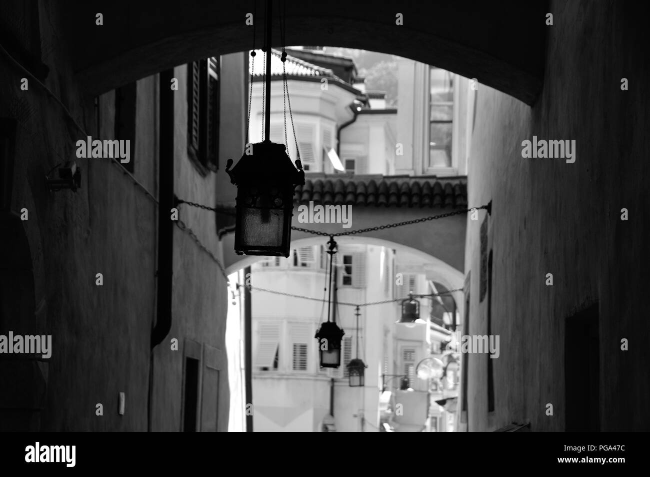 Drei antike Lampen hängen in enge Gasse in der Altstadt von Bozen, Südtirol. Schwarzweiß Stockfoto
