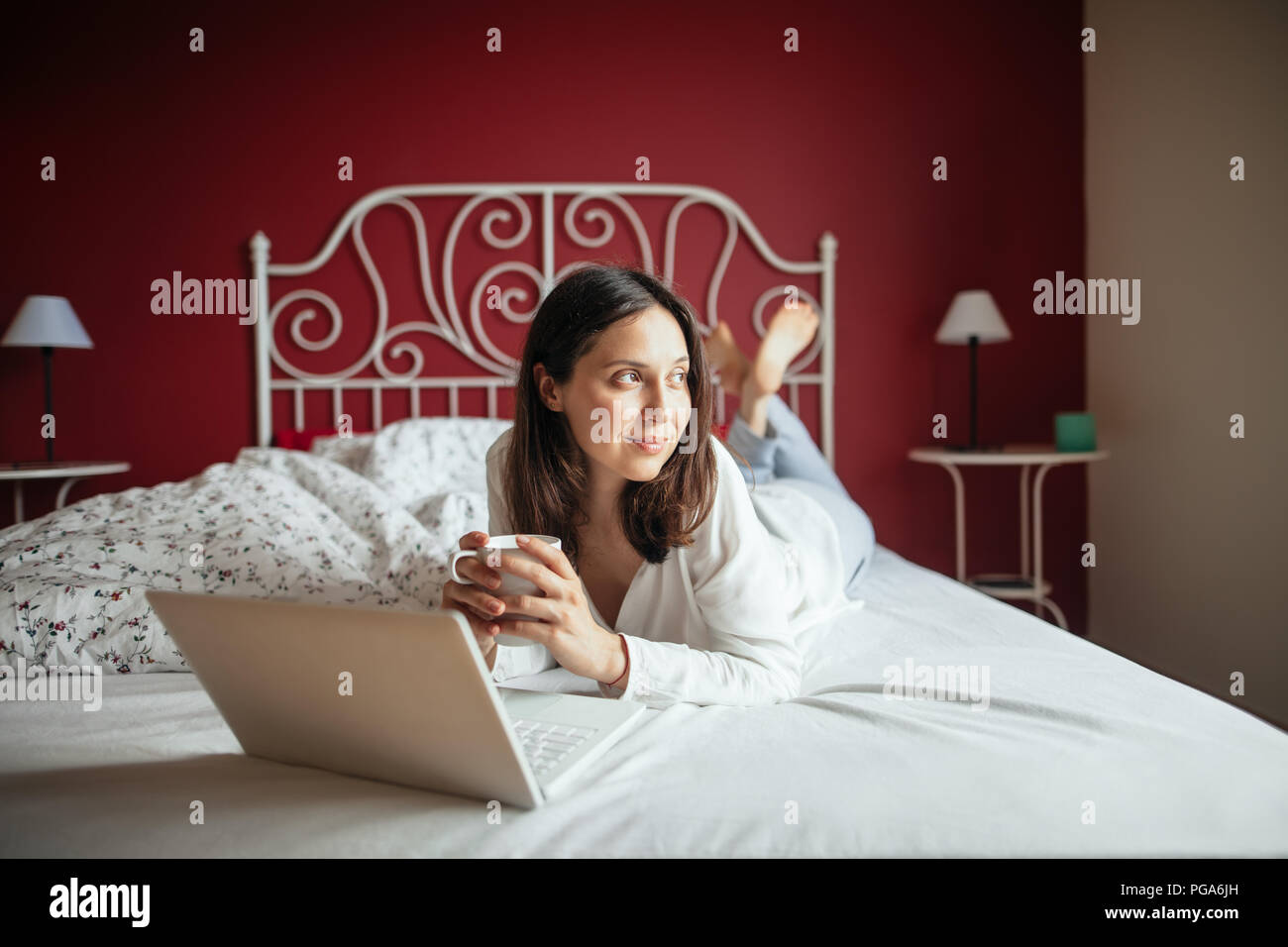 Gerne nachdenklich Frau auf dem Bett und Trinken coffrr mit Laptop zu Hause entspannen. Konzept Rest Stockfoto