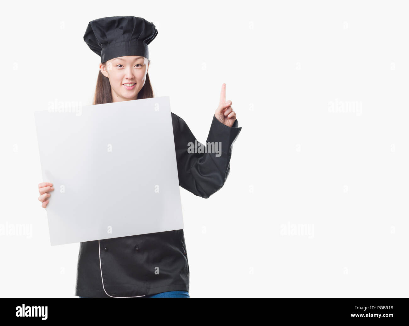 Junge chinesische Frau über isolierte Hintergrund tragen Küchenchef einheitliche Holding banner überrascht mit einer Idee oder Frage Zeigefinger mit glücklichen Gesicht, n Stockfoto