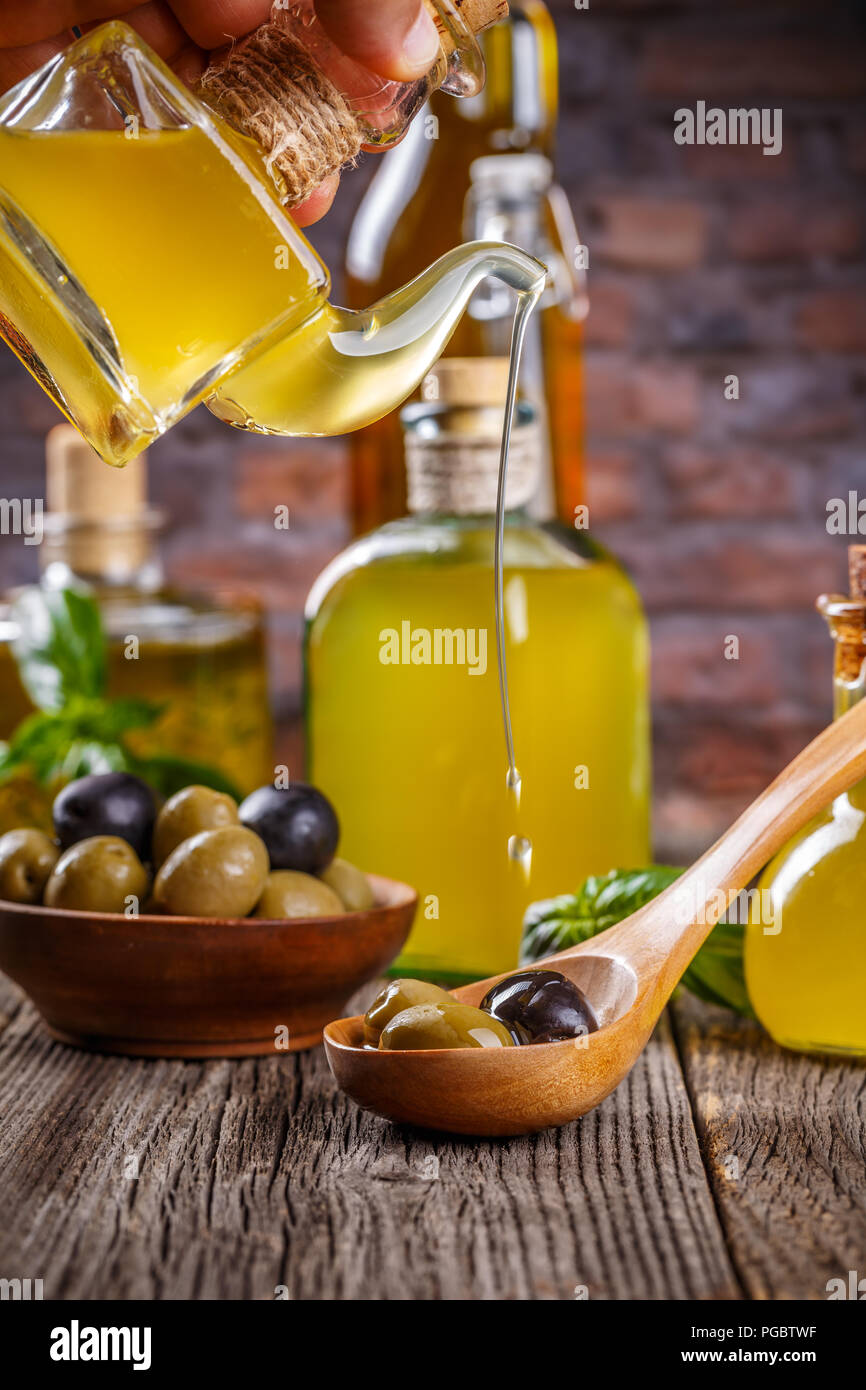 Olivenöl extra vergine Öl fließt auf einer hölzernen Löffel voll von grünen und schwarzen Oliven Stockfoto