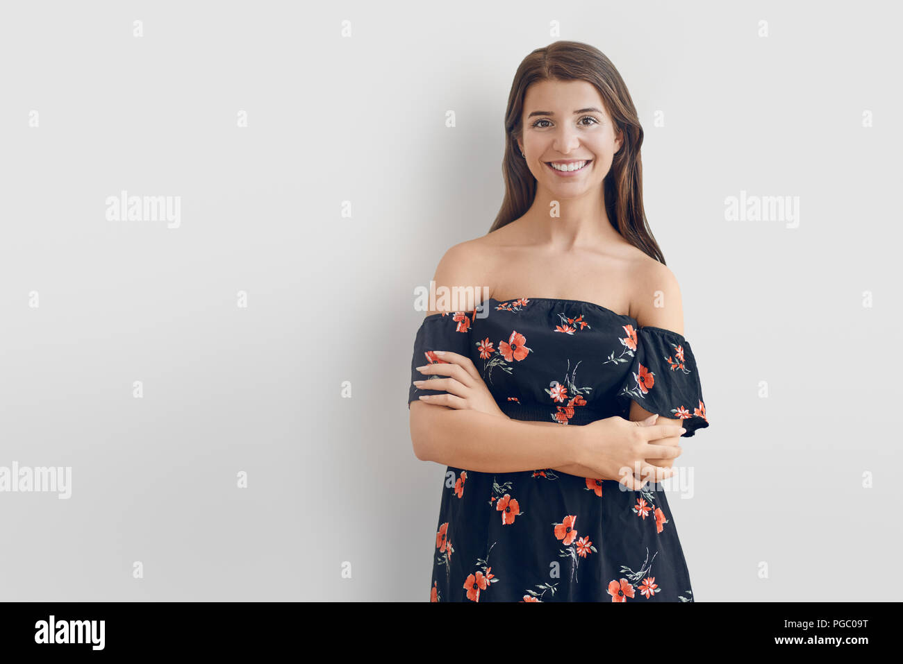 Attraktive stilvolle Frau, die sich von der Schulter Sommer Kleid mit Blumenmuster, gegen einen weißen Hintergrund mit verschränkten Armen an der c suchen Stockfoto