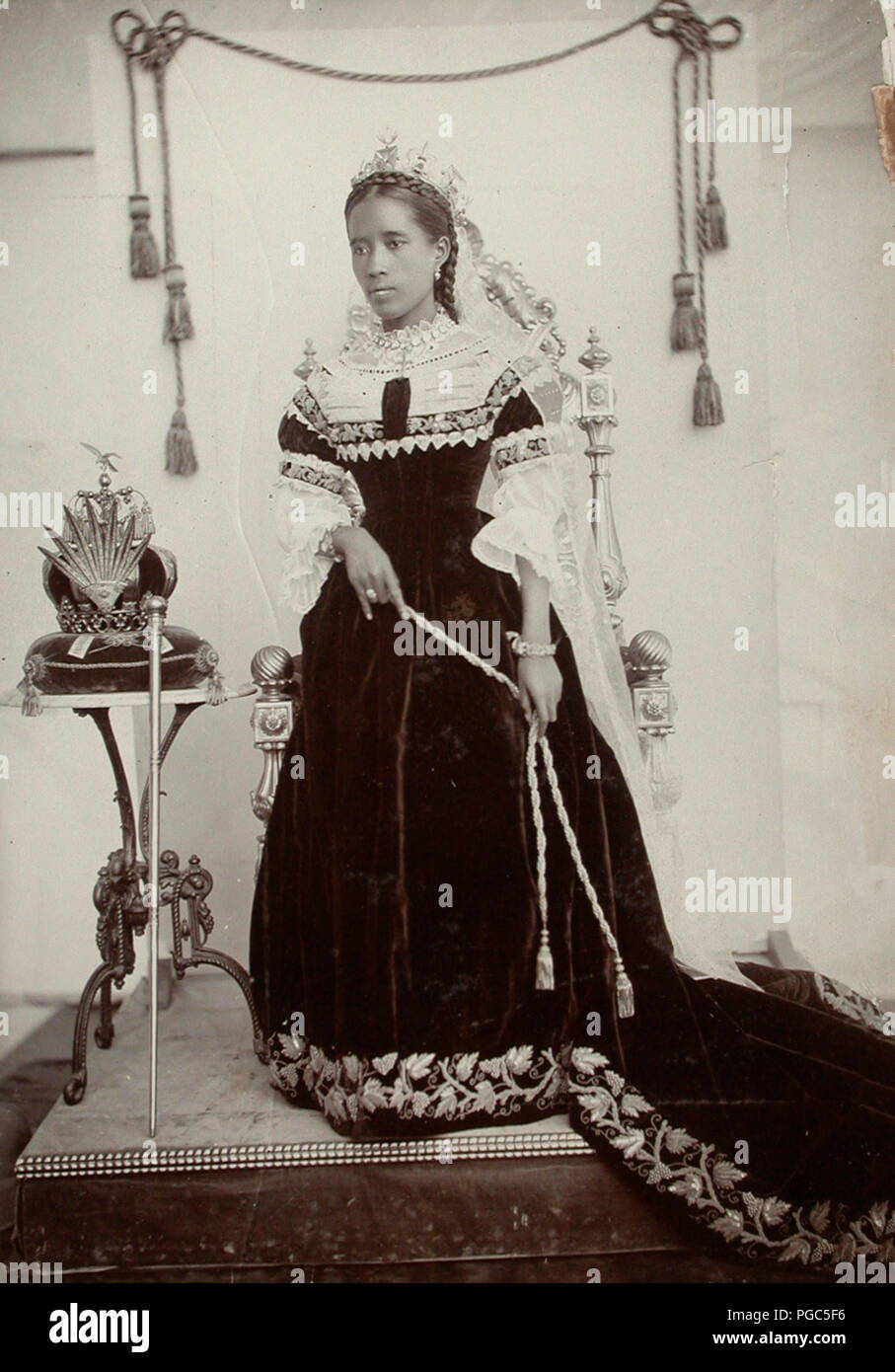 Königin Ranavalona III stand neben einem Thron Tabelle, die ihre Krone auf liegt. Sie trägt einen schönen königlichen Talar, hat einige Stickerei auf. Ihr Haar ist geflochten. Ca. 1890 Stockfoto