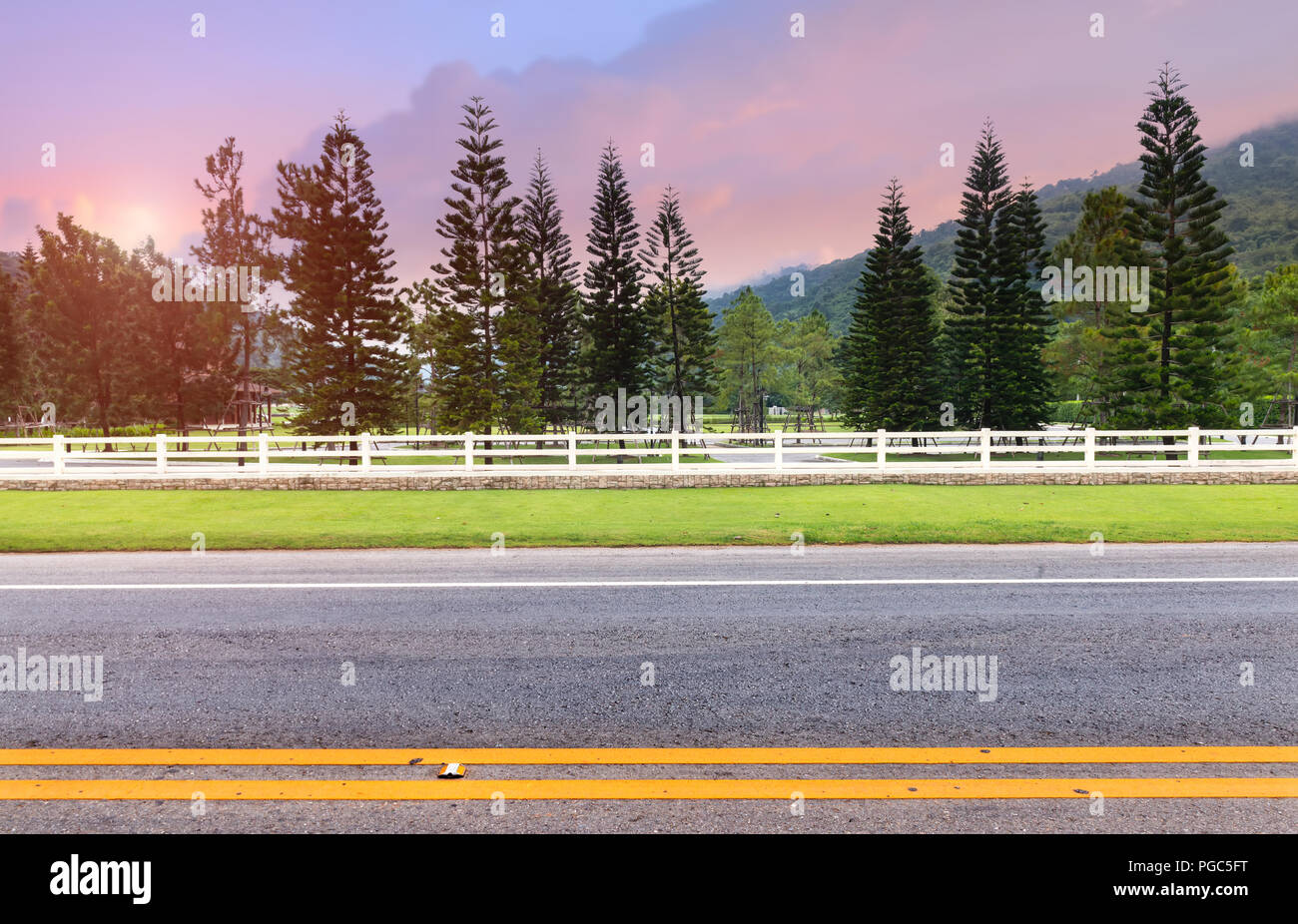 Weißen Zaun am Straßenrand und Kiefer mit pinkfarbenen und blauen Sonnenuntergang Himmel geringer Beleuchtung. Stockfoto