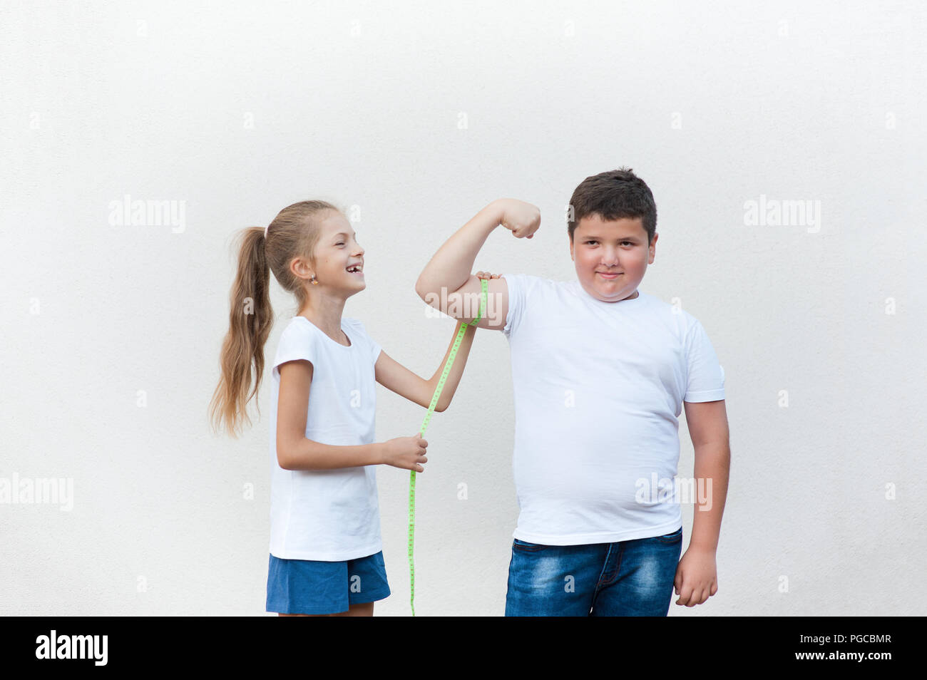 Ziemlich Lachen kaukasischen Thin gesunde Mädchen messen cute Fat Boy Bizeps Muskeln mit Klebeband Stockfoto