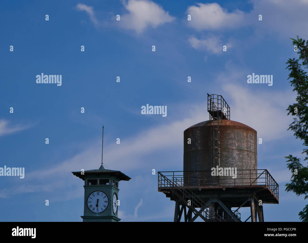 Sehr alte teilweise rostiges Wasser Turm mit einem Clock Tower im Vordergrund und blauen Himmel im Hintergrund Stockfoto