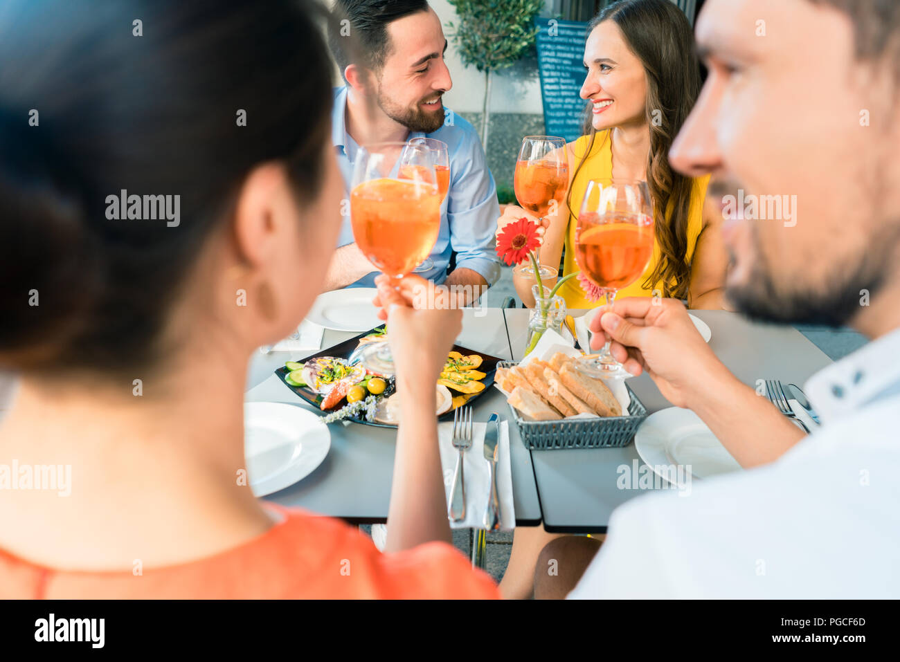 Zwei glückliche junge Paare toasten beim zusammen im Restaurant sitzen Stockfoto