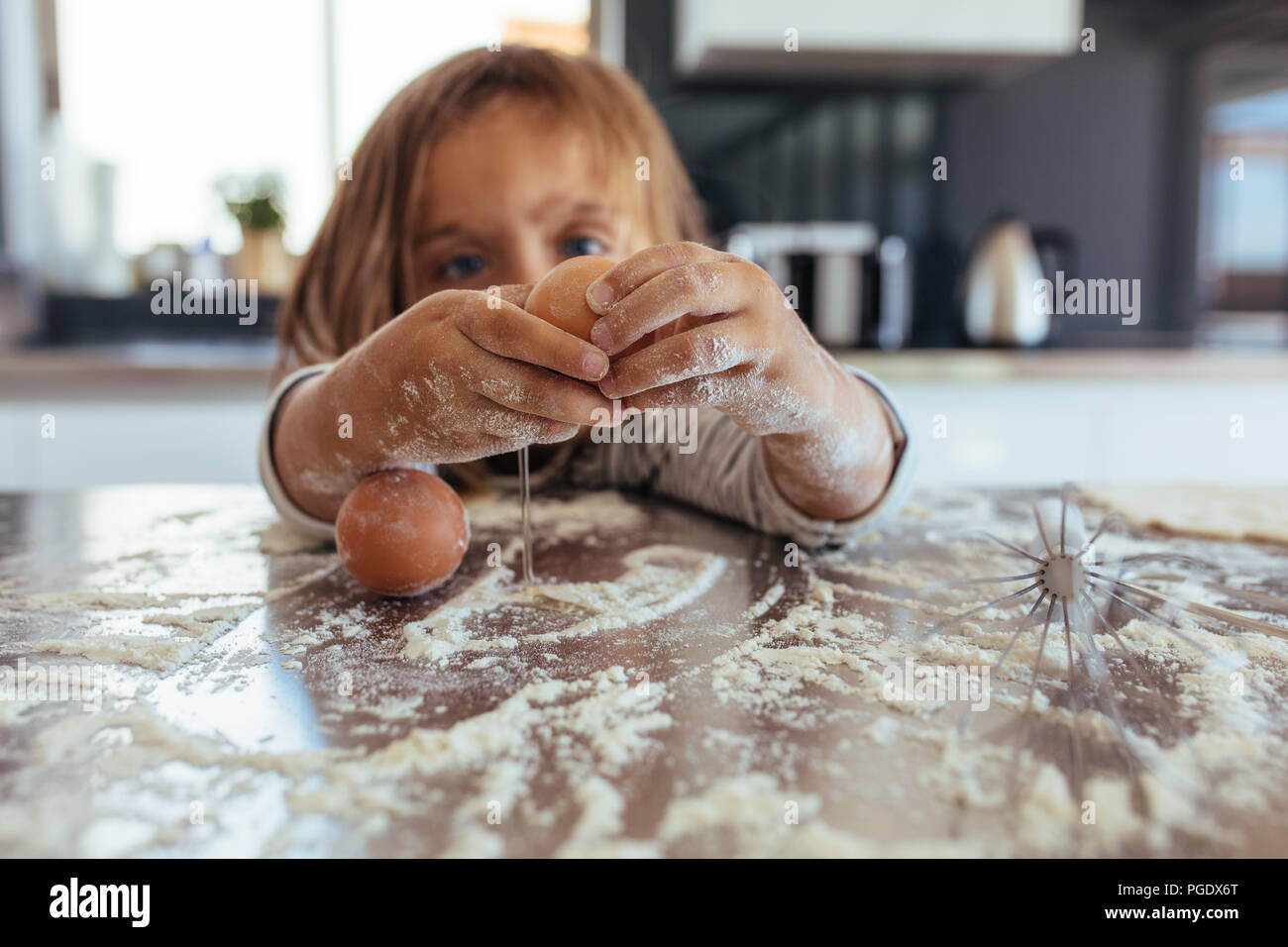 Kleines Mädchen brechen ein Ei auf den Küchentisch mit Mehl bedeckt. Mädchen lernen Kochen in der Küche zu Hause und ein Durcheinander. Stockfoto