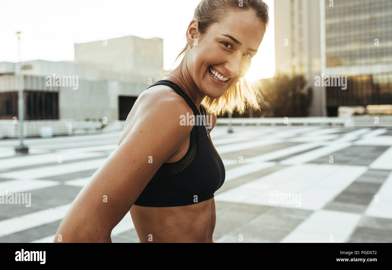 Lächelnd fitness Frau in Trainingskleidung steht auf einer Straße beim morgendlichen Joggen. Frau Athlet Training im Freien in den Morgen mit Sun Flair in Th Stockfoto