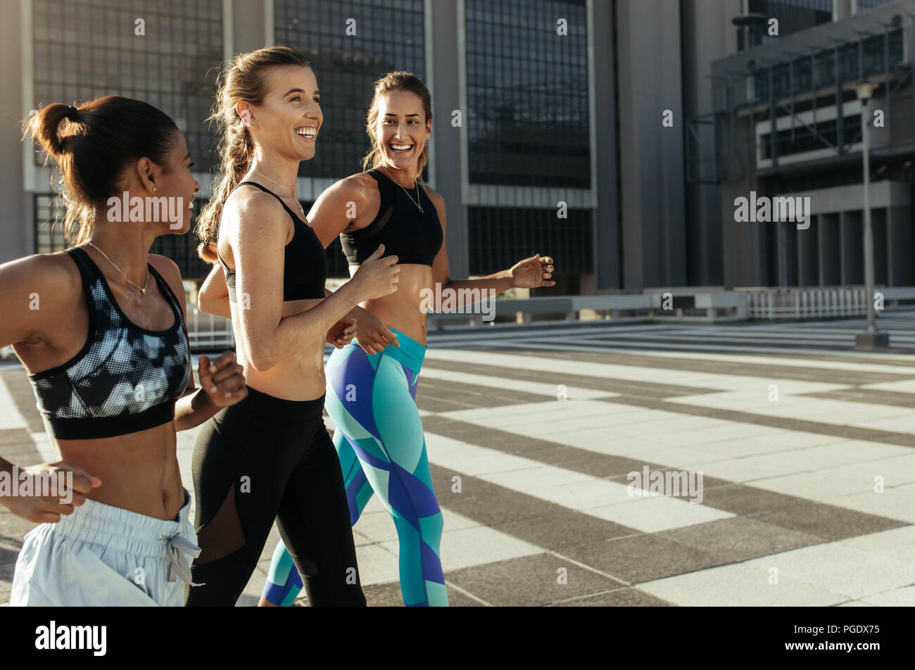 Seitenansicht von drei fitness Frauen Kleidung laufen im Freien. Lächelnd fitness Läufer joggen zusammen in den Morgen. Stockfoto