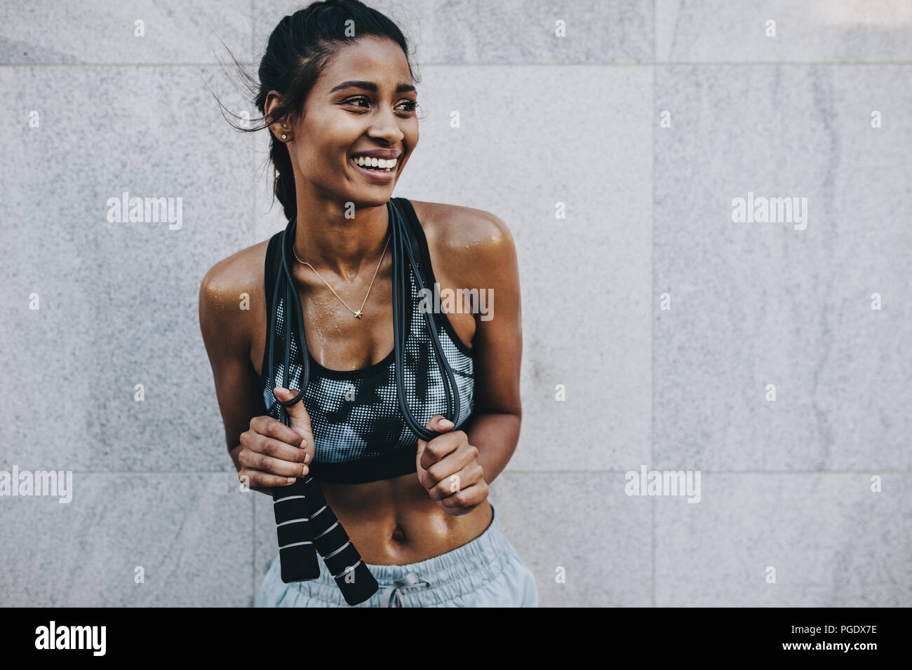 Weibliche Athleten in Fitness Kleidung Entspannung während Ihres Trainings ein Springseil. Lächelnd Fitness im Freien stehende Frau gegen eine Wand gedrückt halten Stockfoto