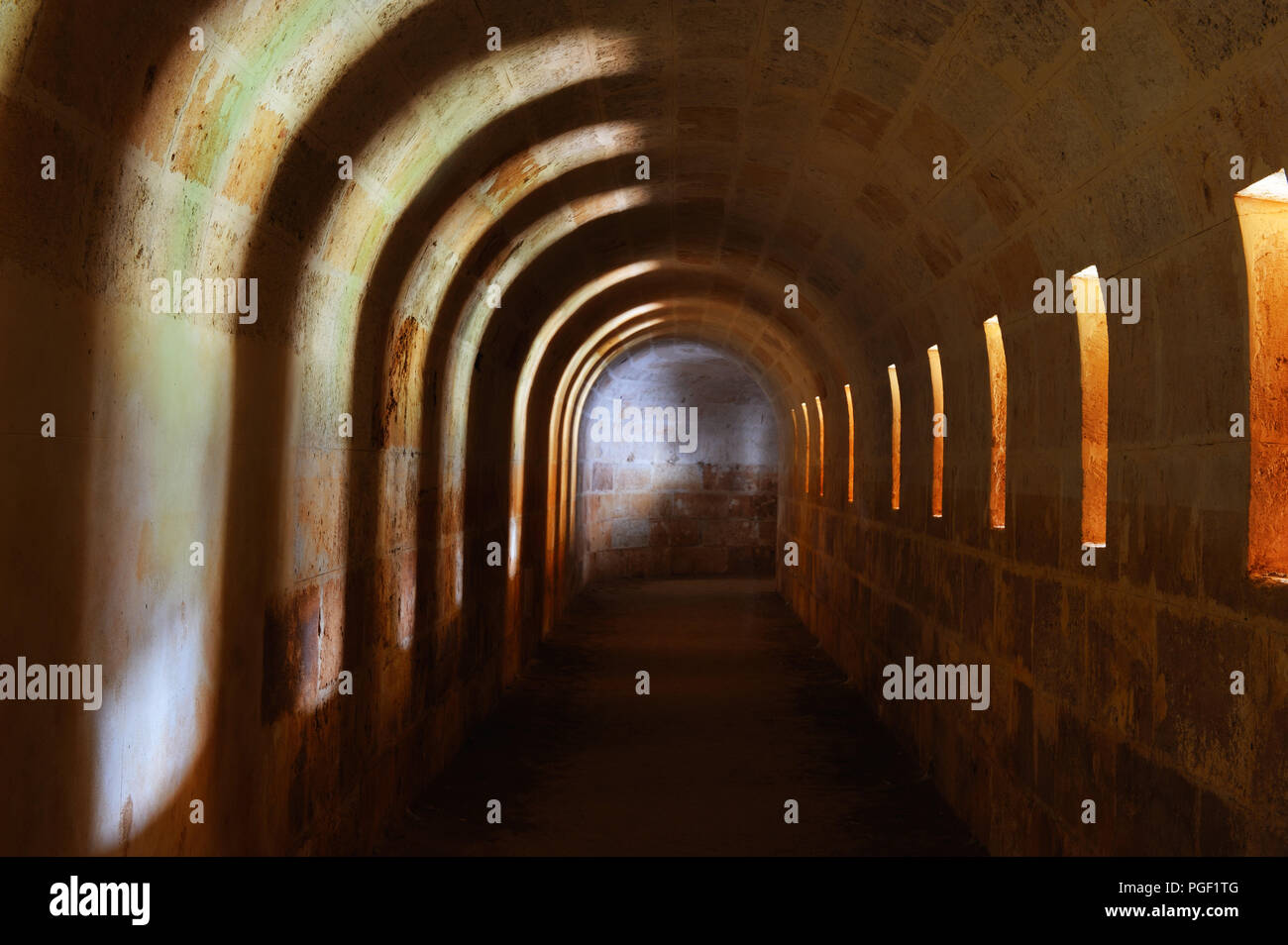 Licht von kanonenluken fällt auf die Geschwungenen Steinmauern ein unterirdischer Gang im La Mola Festung, Menorca, Spanien Stockfoto