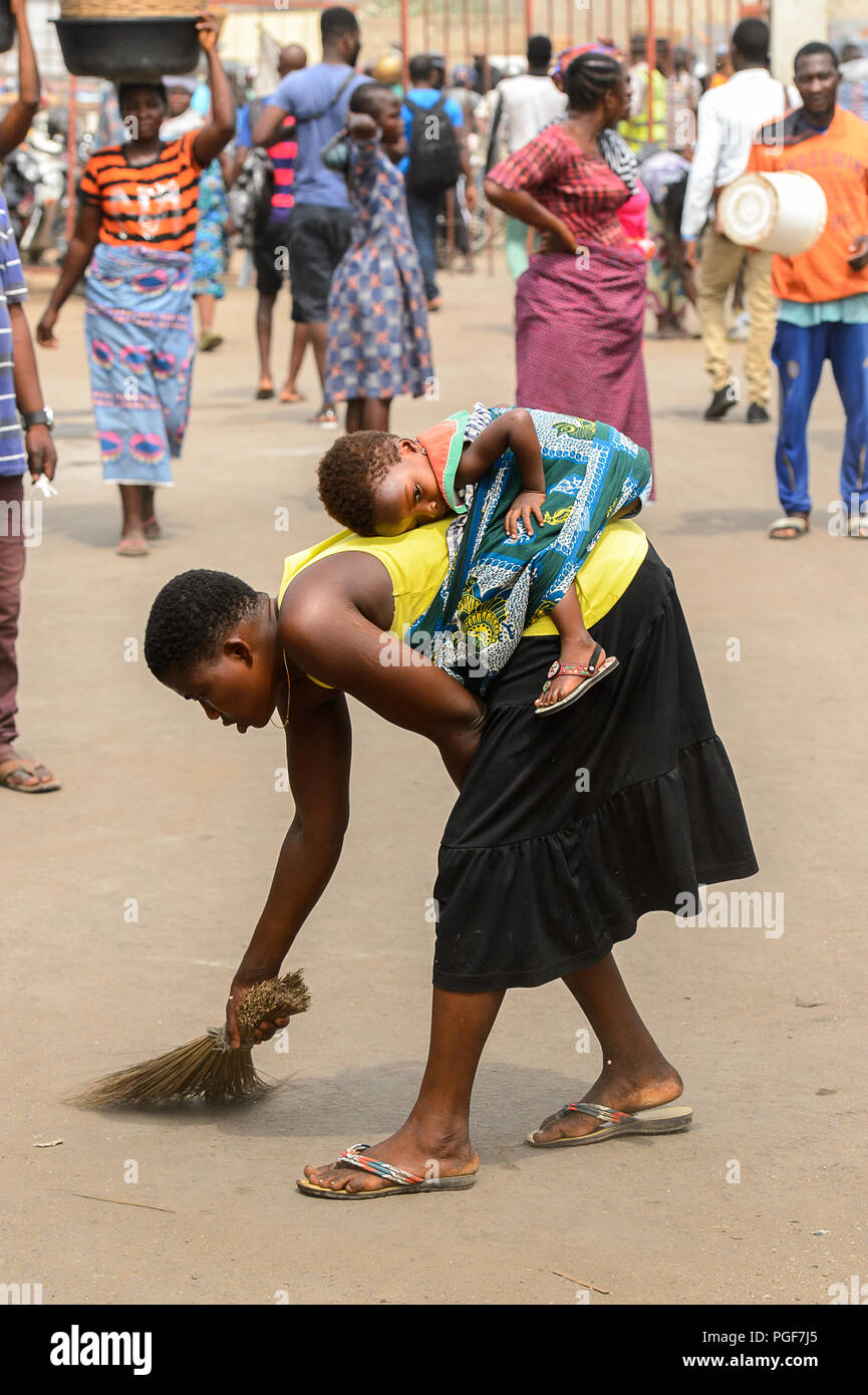 LOME, TOGO - Jan 9, 2017: Unbekannter togoische Frau fegt den Boden und trägt ihr Baby auf dem Rücken an der Lome Port. Togo Leute leiden von Pover Stockfoto