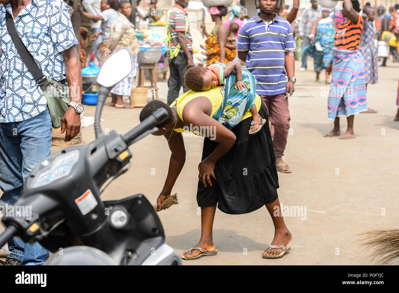 LOME, TOGO - Jan 9, 2017: Unbekannter togoische Frau fegt den Boden und trägt ihr Baby auf dem Rücken an der Lome Port. Togo Leute leiden von Pover Stockfoto
