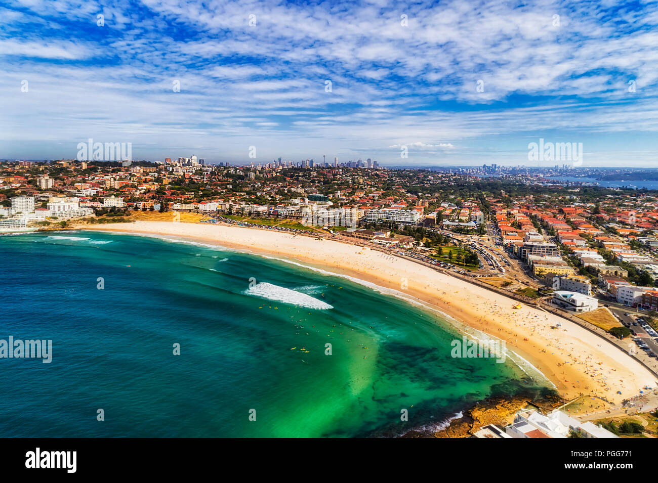 Alle weltberühmten Bondi Beach Sydney breiten Streifen von sauberem Sand mit flachen Smaragdgrün blaues Wasser mit weit entfernten Stadt CBD Türme am Horizont unter blauem Summe Stockfoto