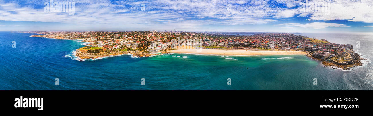 Berühmten Sydney Bondi Beach zwischen Sandstein Vorgewende aus dem offenen Meer gesehen auf einem breiten Küstenstreifen der Großraum Sydney mit Stadt CBD Türme am Horizont. Stockfoto