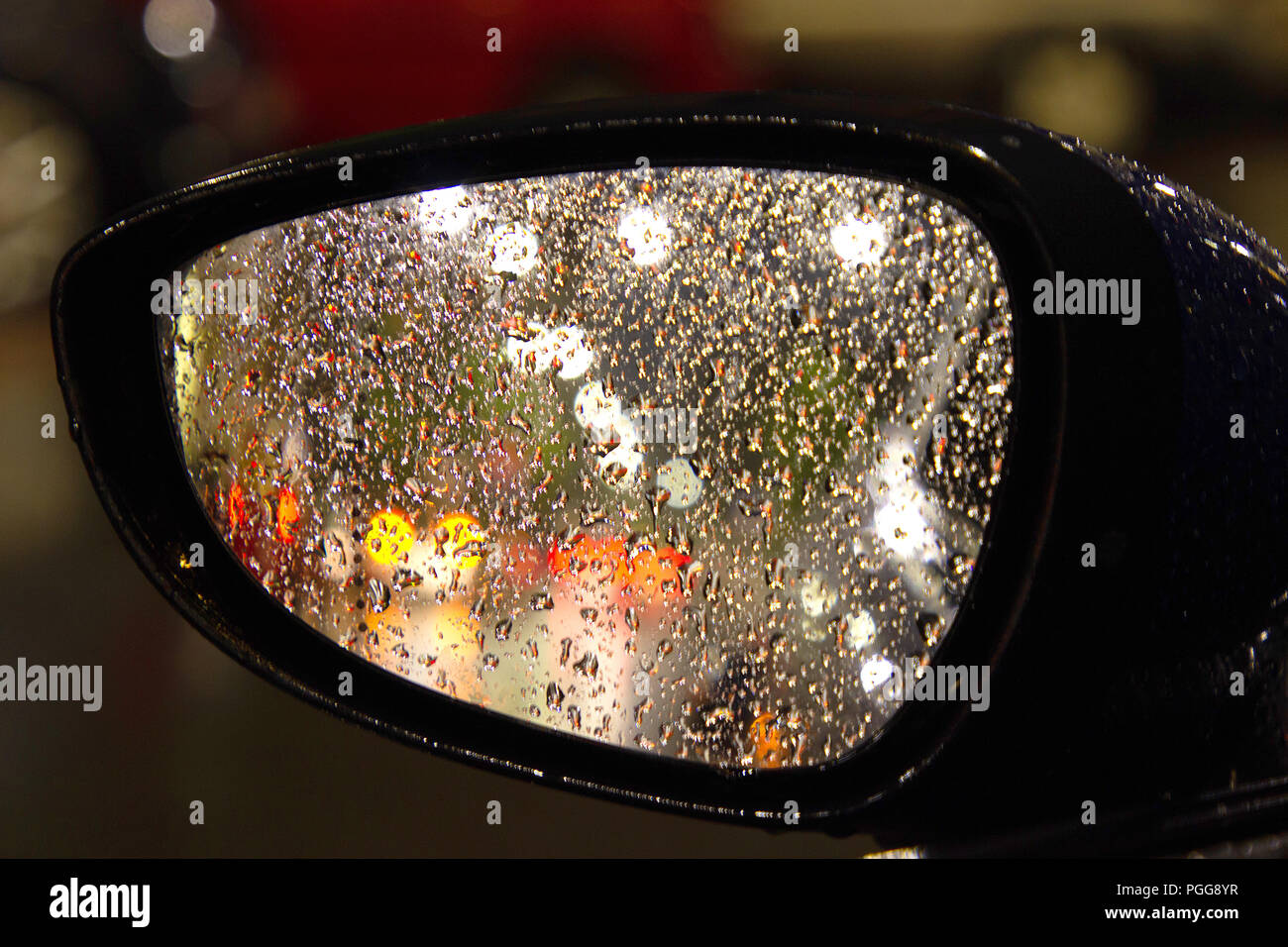 Ein künstlerisches Foto einer Straßenbeleuchtung im Regen durch einen seitlichen Blick auto Spiegel in der Nacht Stockfoto