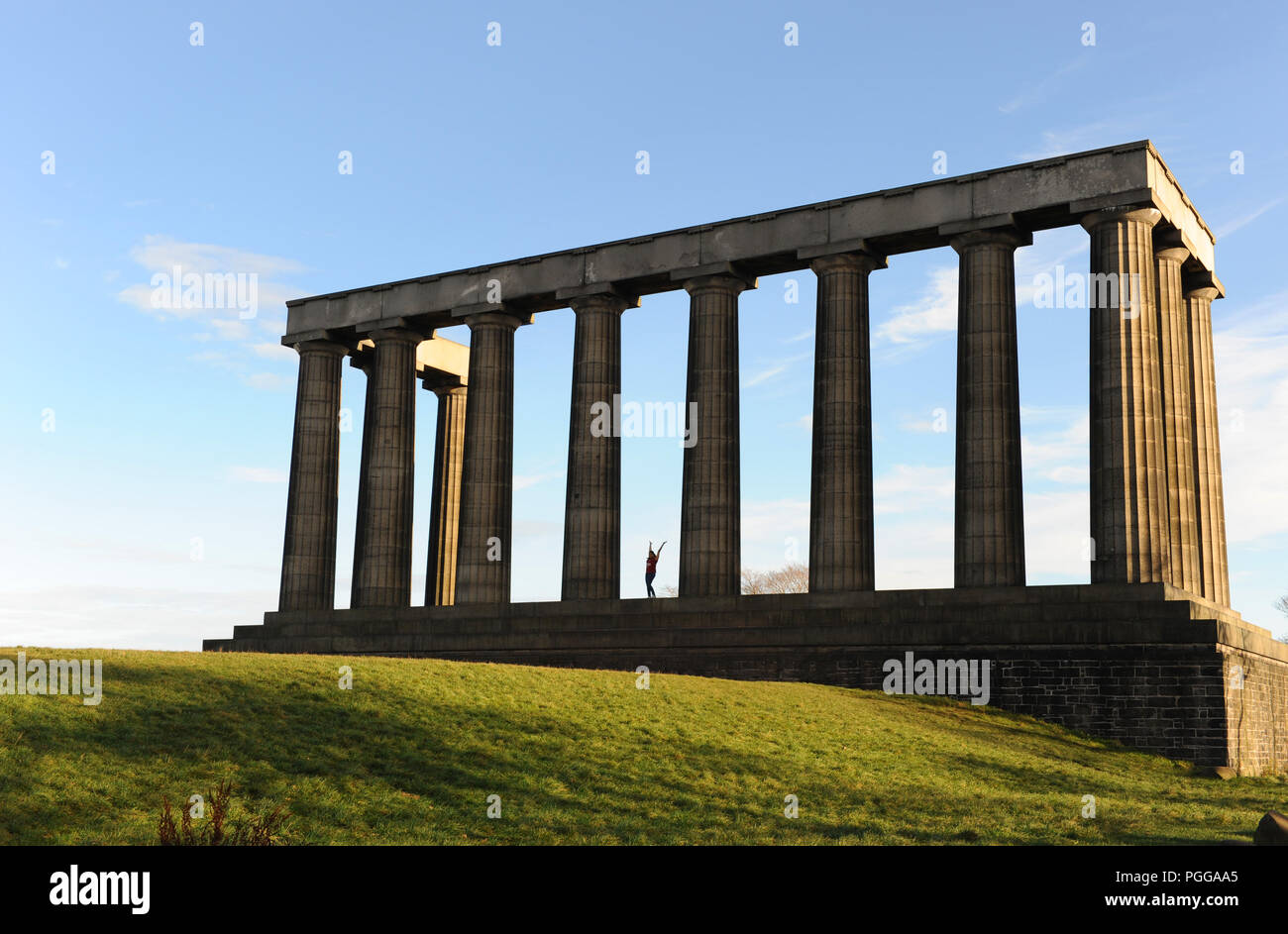 Eine junge Frau hebt ihre Arme vor Freude zwischen Kolonnen auf dem Unfinished National Monument of Scotland auf Calton Hill, Edinburgh, Schottland Stockfoto