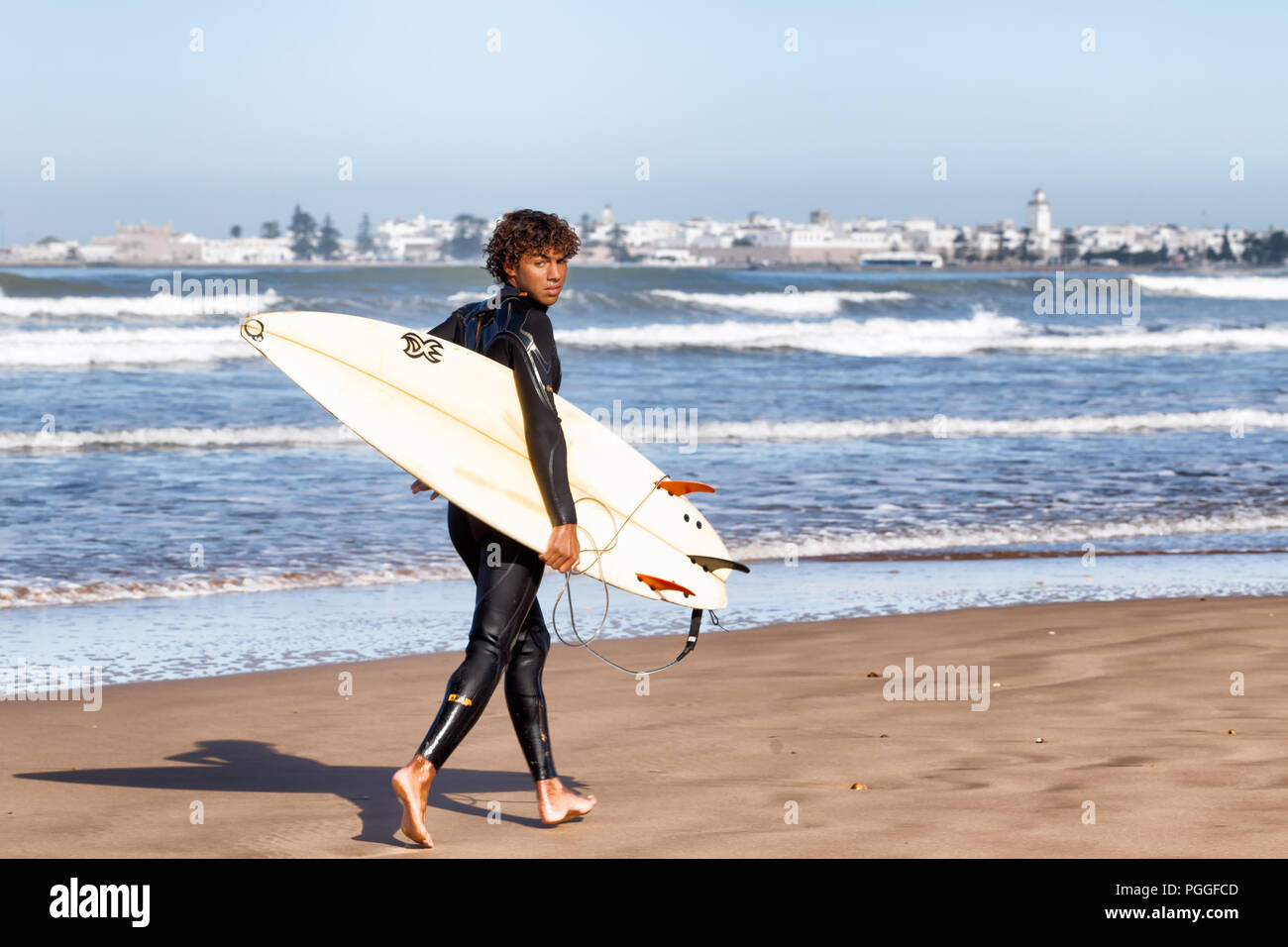 ESSAOUIRA, MAROKKO - Dec 22, 2012: unbekannter Surfer mit einem Surfbrett auf dem Sand am Wasser entlang in Essaouira, Marokko, gelegen am Atlantik c Stockfoto