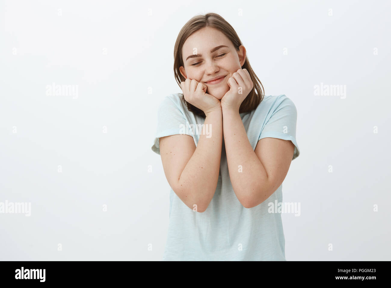 Süße niedliche Mädchen erinnert an Amüsanten schönen Moment verträumt und Glücklich schließen die Augen vor Freude Lächeln breit schiefen Gesicht auf den Händen stehen begeistert und romantisch auf weißem Hintergrund Stockfoto