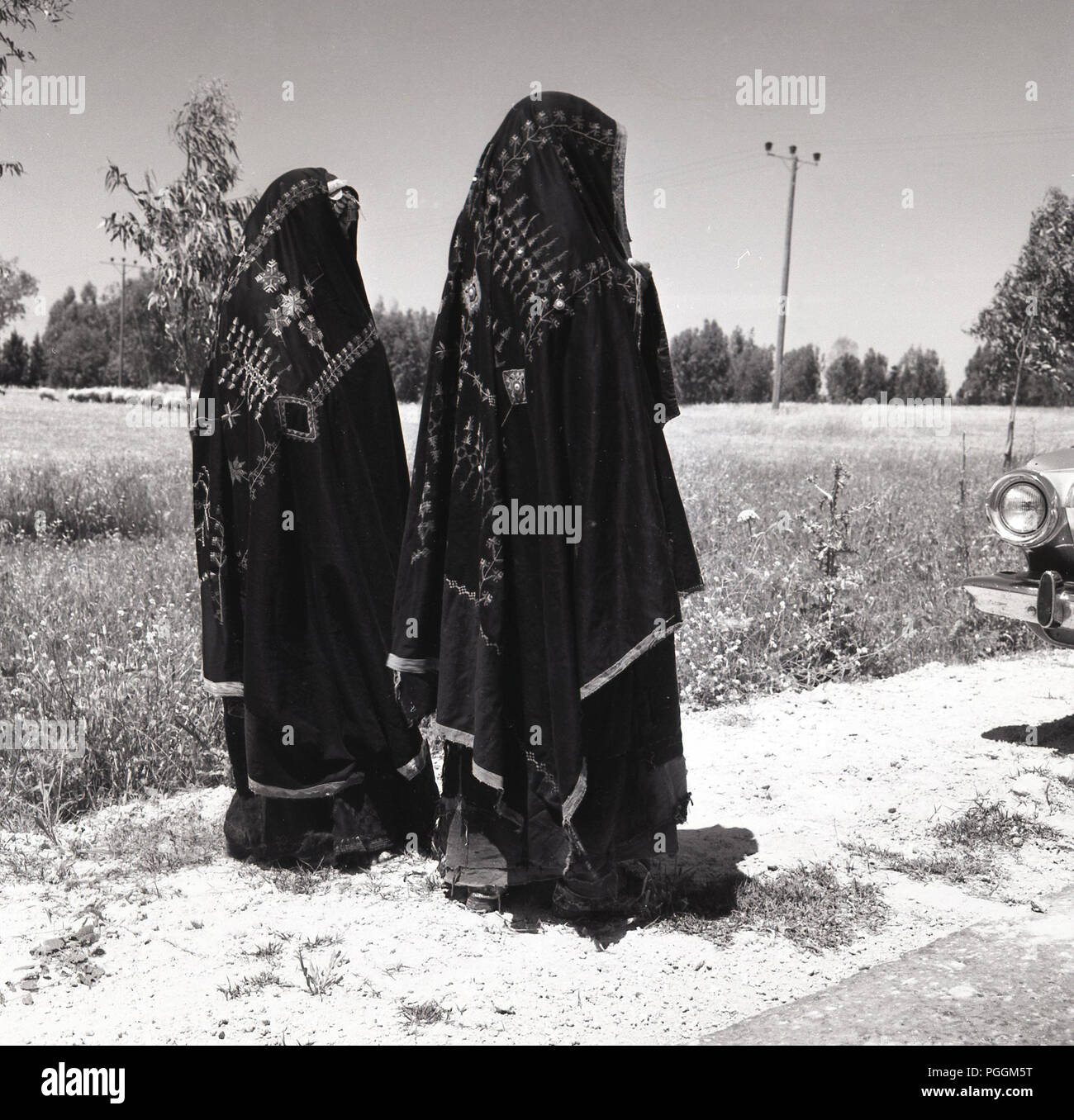 1950, historische, Ansicht von hinten von zwei Beduinen Frau entlang einem strassenrand in traditionellen und unverwechselbaren Palnestinian bestickte Kleidung, mit Schleiern oder Mützen auf ihren Köpfen, und Israel. Stockfoto