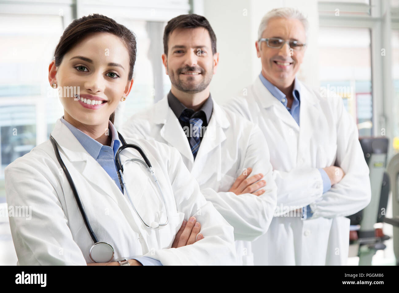 Glücklich erfolgreiches medizinisches Team in einem Krankenhaus in Ihren weißen Kittel mit verschränkten Armen in einem rückläufigen gestaffelte Reihe mit Fokus auf eine attraktive Stockfoto