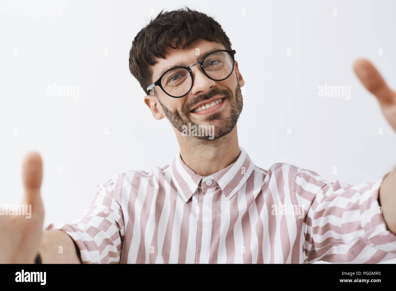 Headshot von zufrieden und nette gut aussehende glücklich kaukasischen Kerl bärtigen mit modischer Frisur in kühlen trendigen gestreiften Hemd ziehen Hände towads Kamera als ob man selfie freudig lächelnd Stockfoto