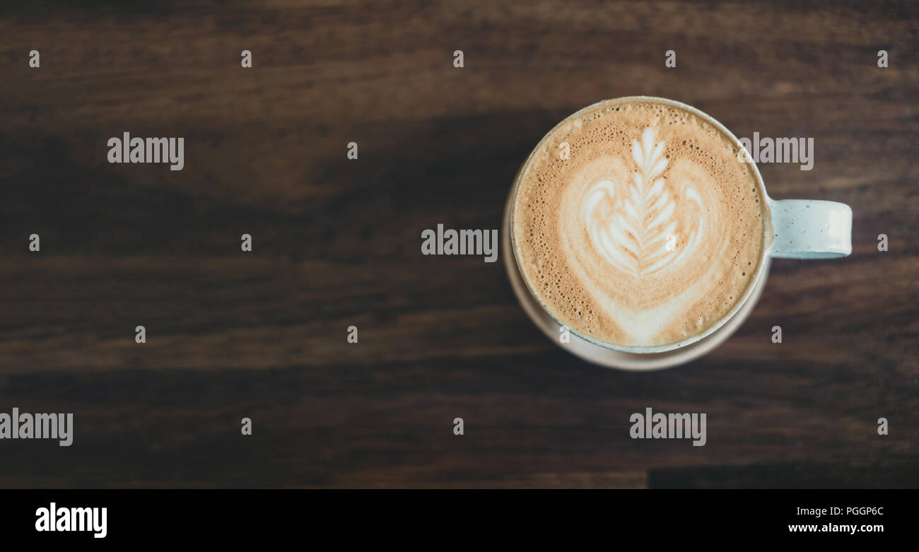Blick von oben auf die heißen Cappuccino Tasse auf Holz- Fach mit latte Kunst auf Holz Tisch im Cafe, Banner Größe Essen und Trinken Konzept. Kopieren sie Raum lassen für Addi Stockfoto