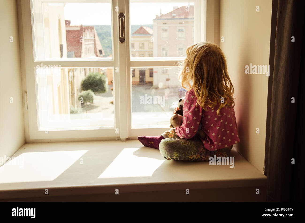 Kleine blonde Mädchen saßen und über Fenster Stockfoto